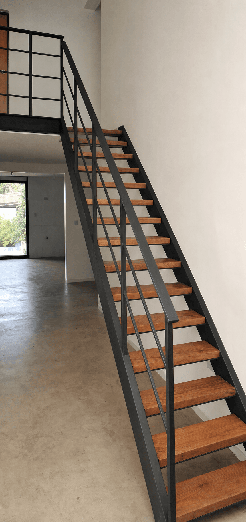 Escalera recta de hierro negro con peldaños de madera instalada en una vivienda
