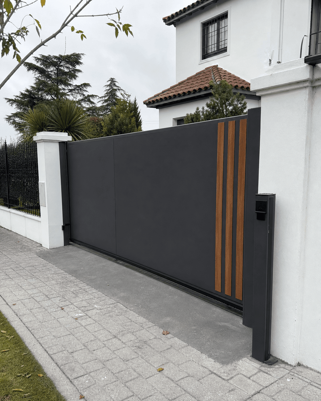 Portón corredizo de chapa gris con detalles verticales en madera instalado en una vivienda