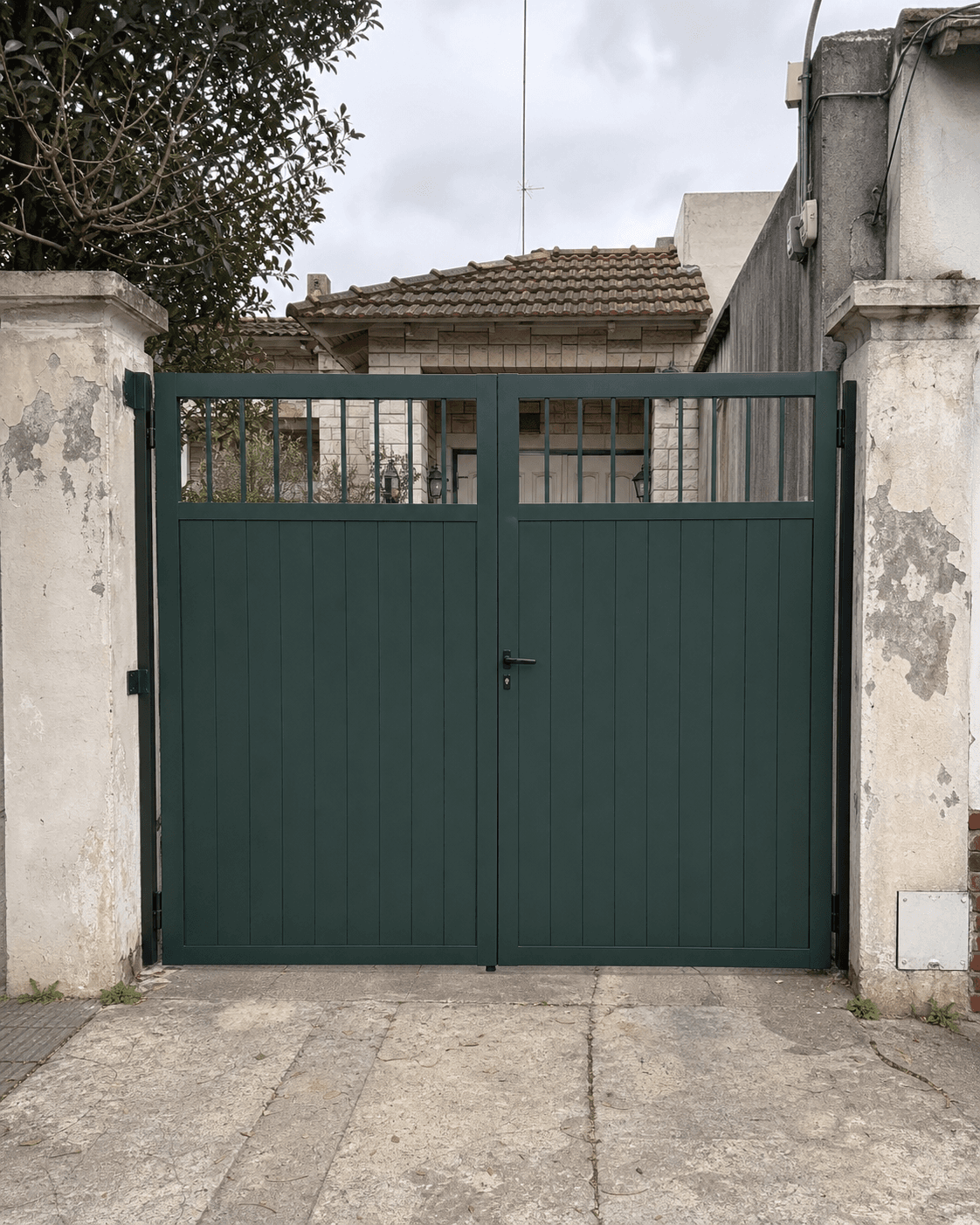 Portón de acero verde de dos hojas con barrotes superiores instalado en una vivienda
